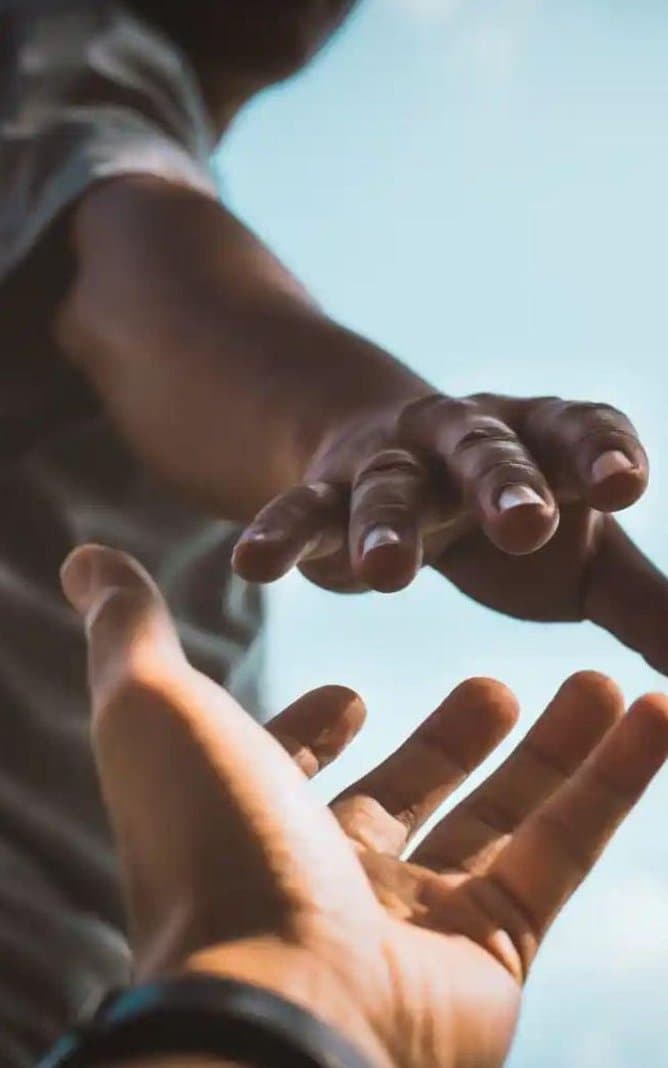 A Black hand reaching down from open sky to clasp another person's outstretched hand