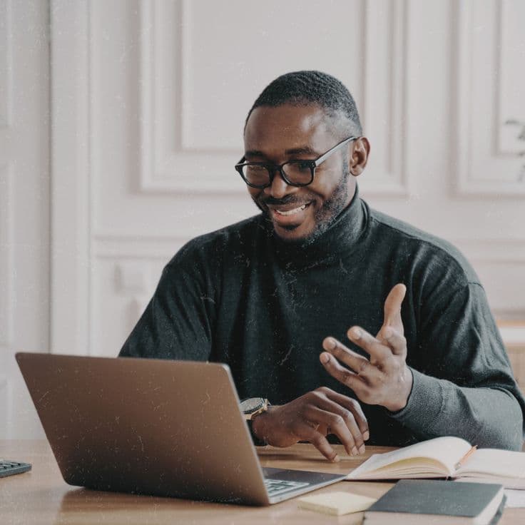 A smiling Black man in glasses talking with his provider over a video call at home